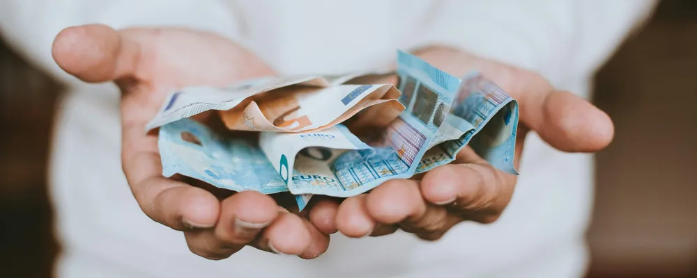 A person holding euro banknotes, symbolising charitable giving